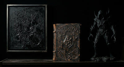 A dark collector shelf with a black art print, an ancient book and a shadowed statue