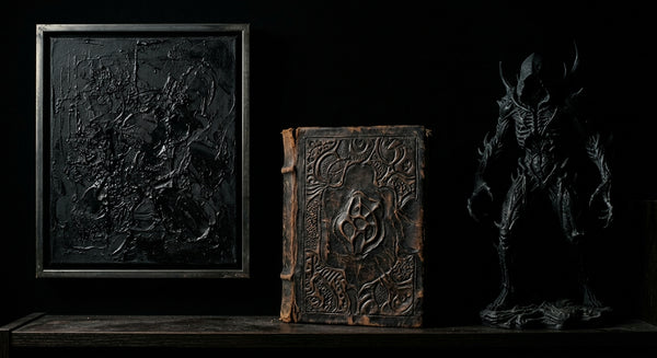 A dark collector shelf with a black art print, an ancient book and a shadowed statue