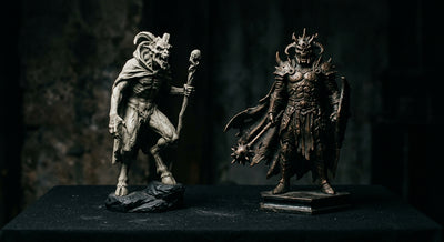 Two horror collectible statues of different materials side by side, one stone-grey and one metallic bronze
