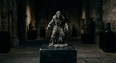 An aged horror resin collectible statue with patina on a pedestal in a dim gothic gallery